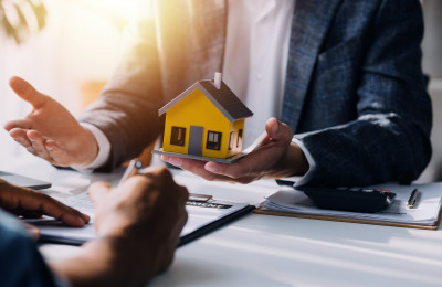 Makler hält gelbes Modellhaus hoch