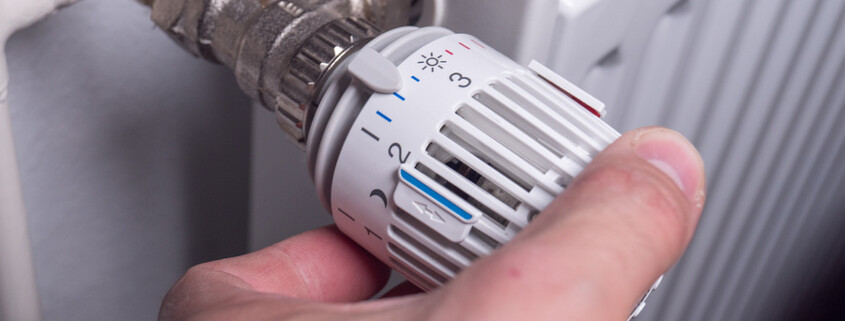 Mann dreht am Thermostat einer Heizung