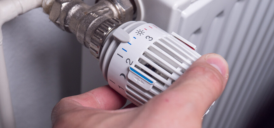 Mann dreht am Thermostat einer Heizung