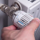 Mann dreht am Thermostat einer Heizung