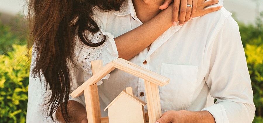 Junges glückliches Paar mit einem Modellhaus aus Holz