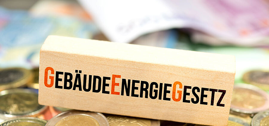 Holzblock mit der Aufschrift Gebäudeneergiegesetz liegt auf Münzen