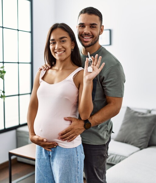 Schwangere Frau hält Hausschlüssel und wird vom Partner umarmt