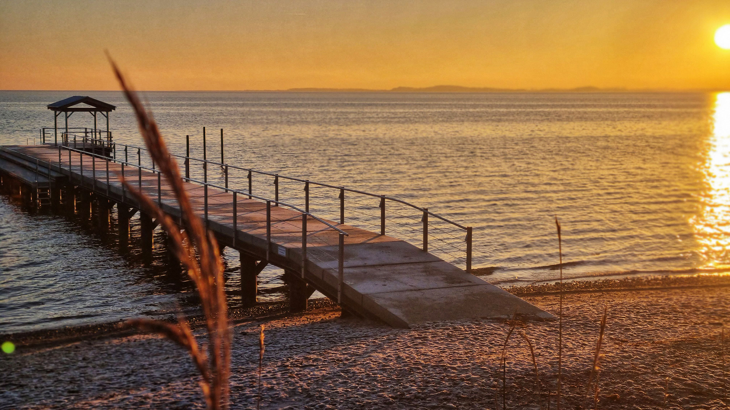 Sonnenuntergang über einem See mit einer Brücke, die zum Wasser führt.