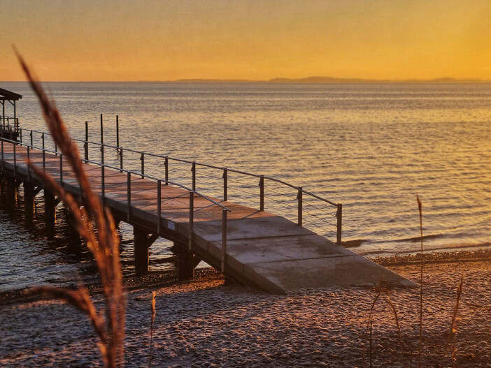 Sonnenuntergang über einem See mit einer Brücke, die zum Wasser führt.