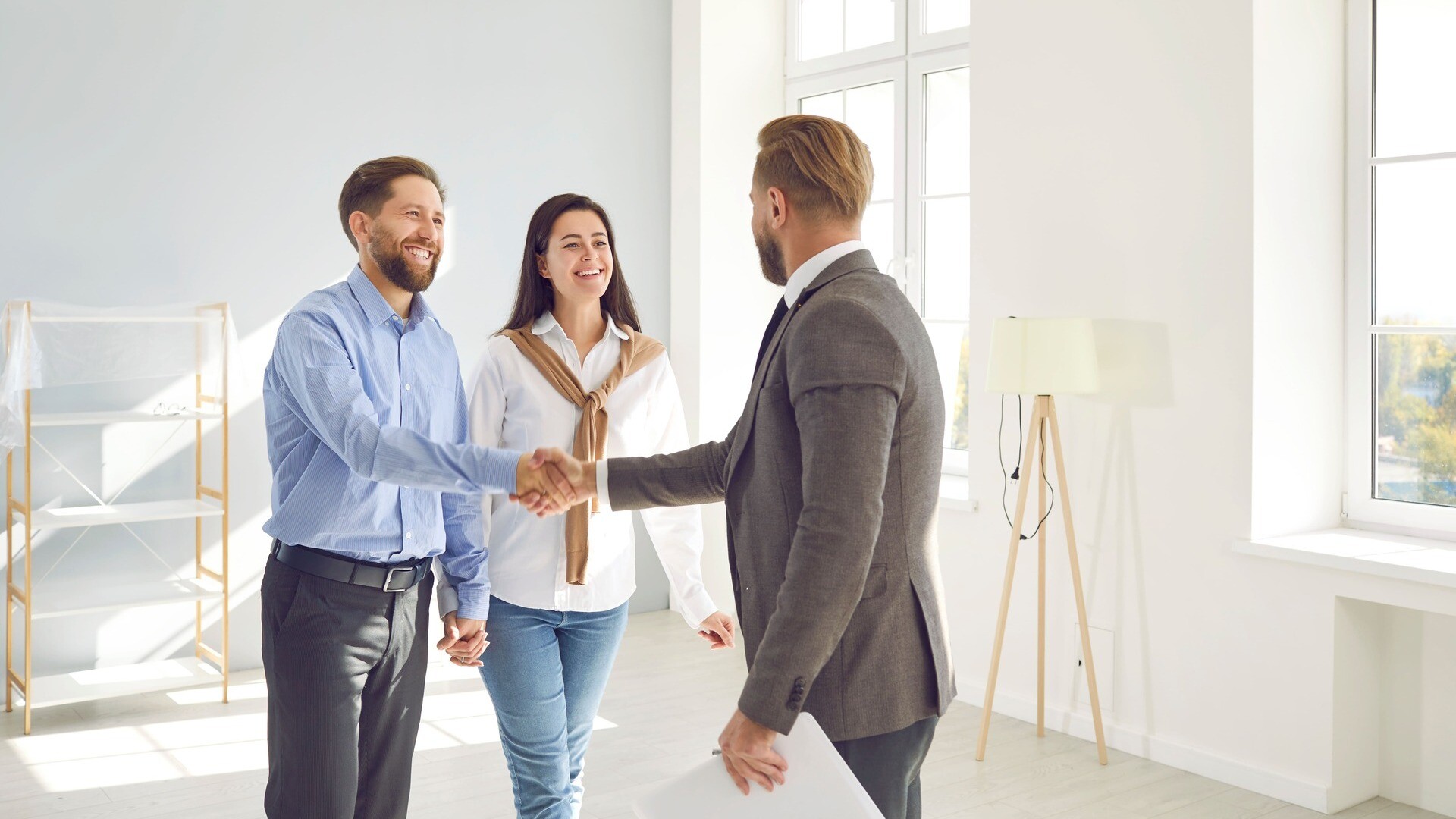 Ein Makler schüttelt einem Paar nach erfolgreichem Immobilienverkauf die Hand