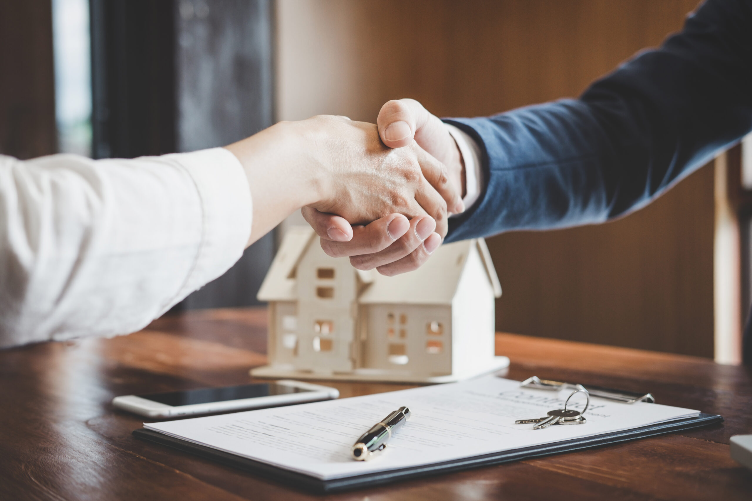 Zwei Personen geben sich über Vertrag und Modellhaus die Hand.