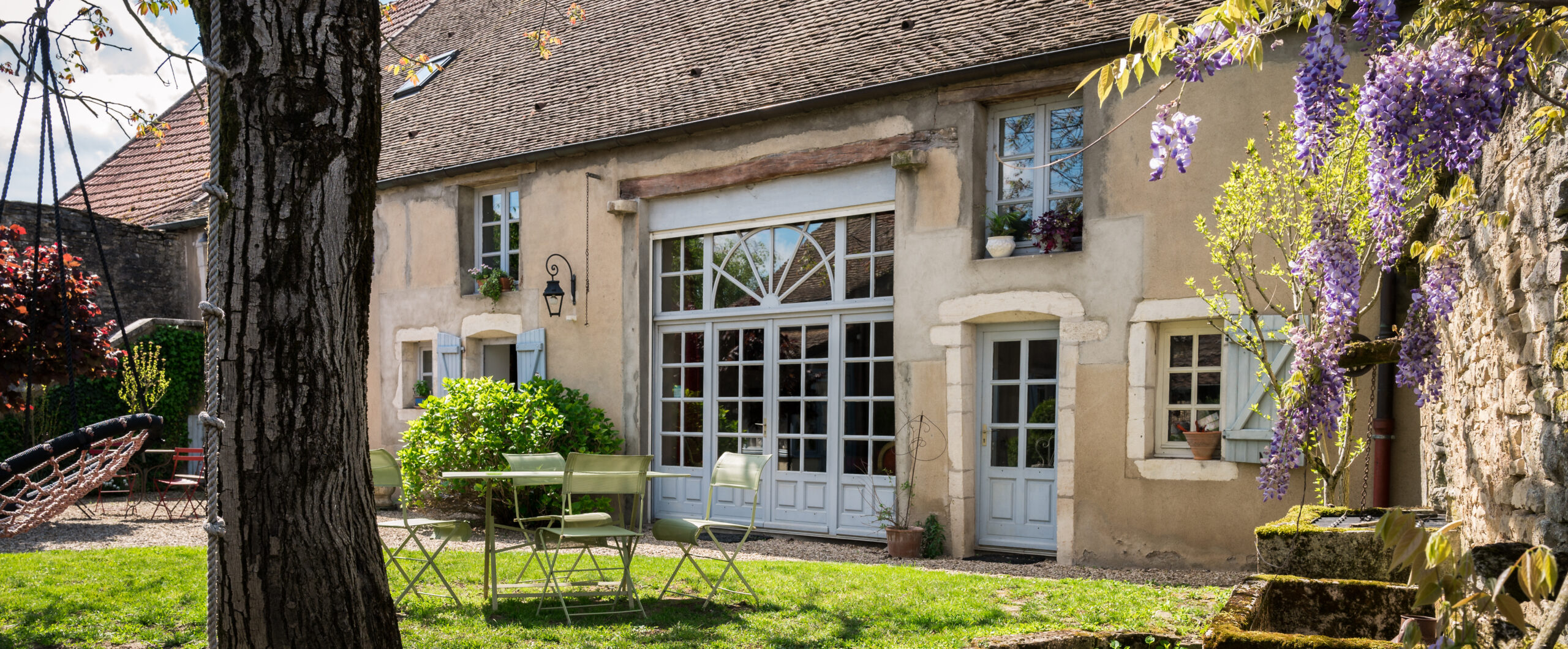 Rustikales Haus mit großen Fenstern und blühendem Glyziniengarten.