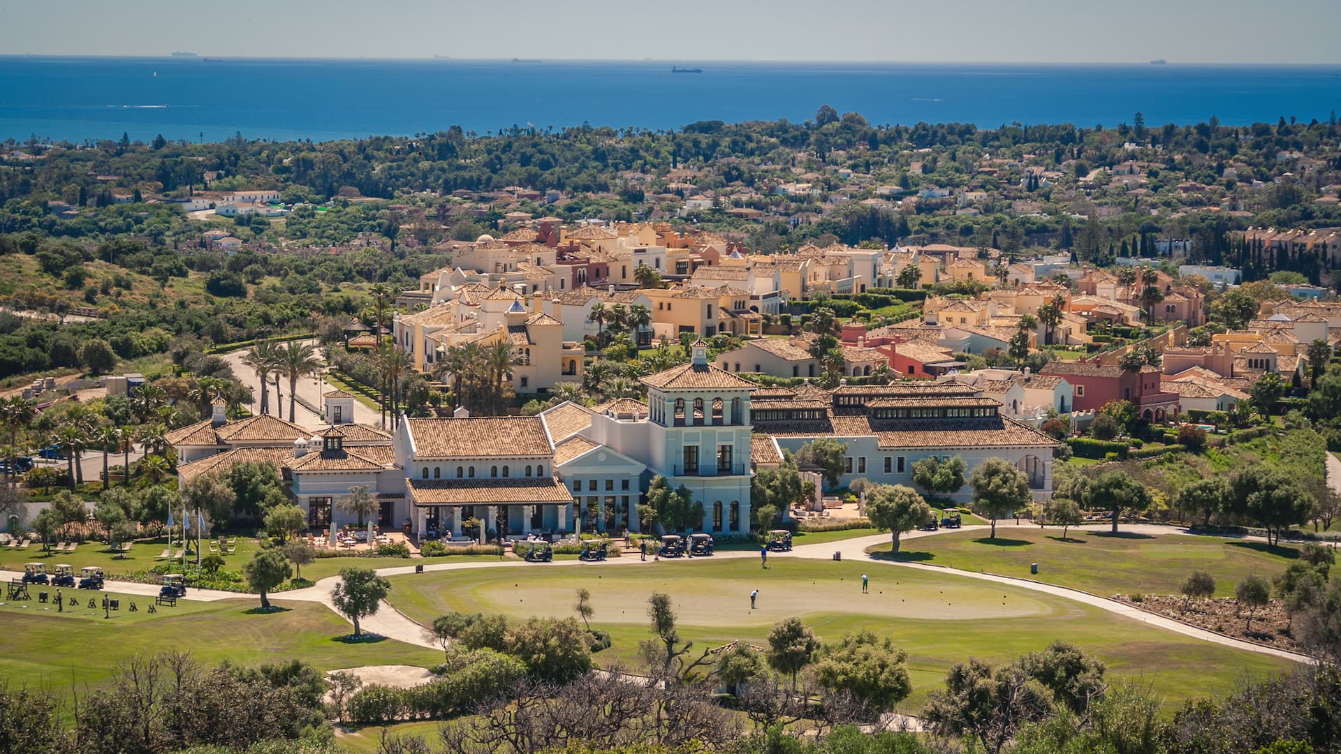Golfplatz, Clubhaus und Villen mit Meer im Hintergrund bei Sonne