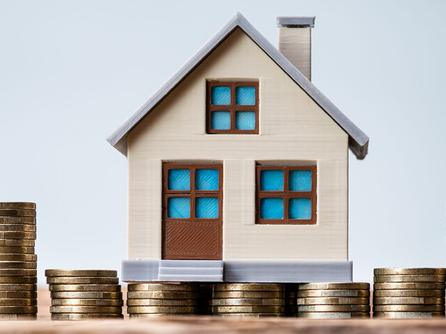 Miniaturhaus und Münzstapel als Symbol für die Inflation