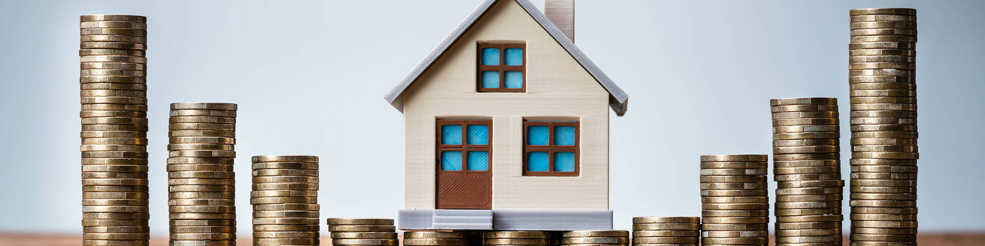 Miniaturhaus und Münzstapel als Symbol für die Inflation