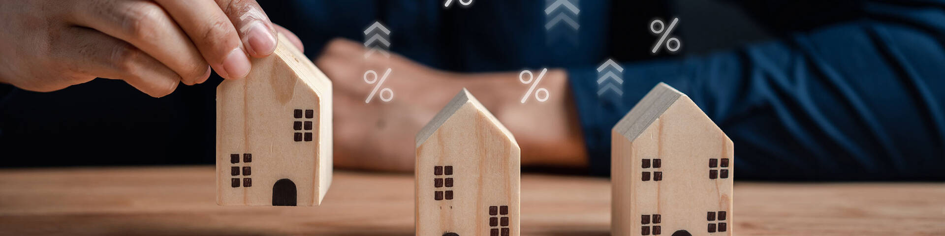 Kauf und Verkauf bei gestiegen Zinsen: Man mit Modellhäusern und Prozentzeichen