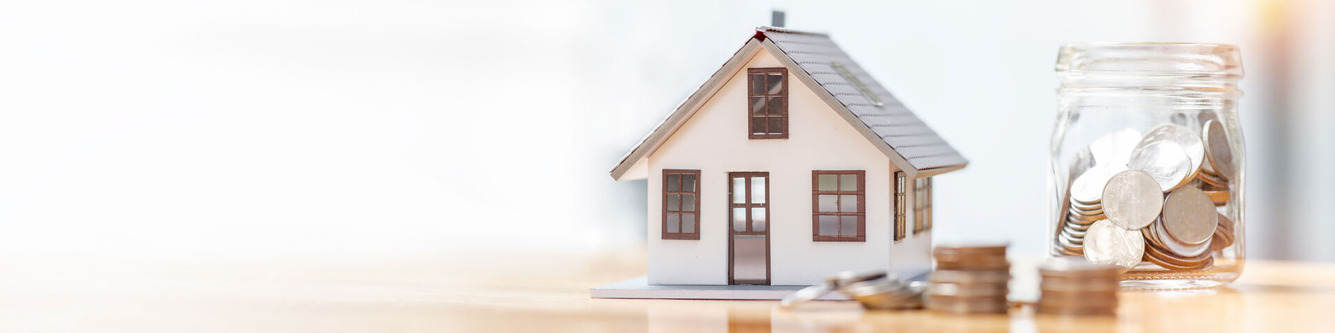 Modellhaus und Münzglas als Symbol zum Investieren in Immobilien