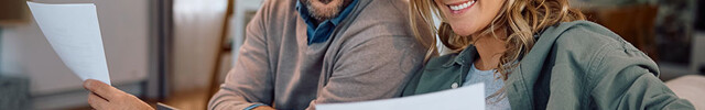 Ehepaar sitzt auf der Couch mit Laptop und informiert sich über Hausversicherungen