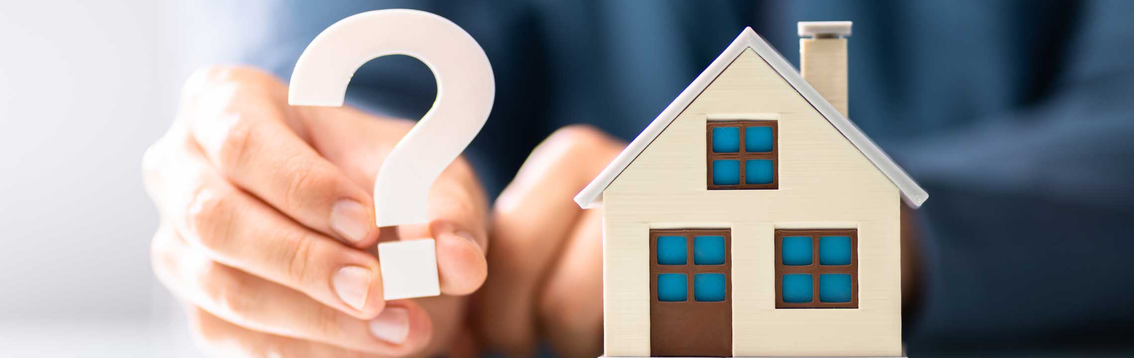 Person hält Fragezeichen neben Modellhaus: Symbol für Änderungen in der Branche 2026