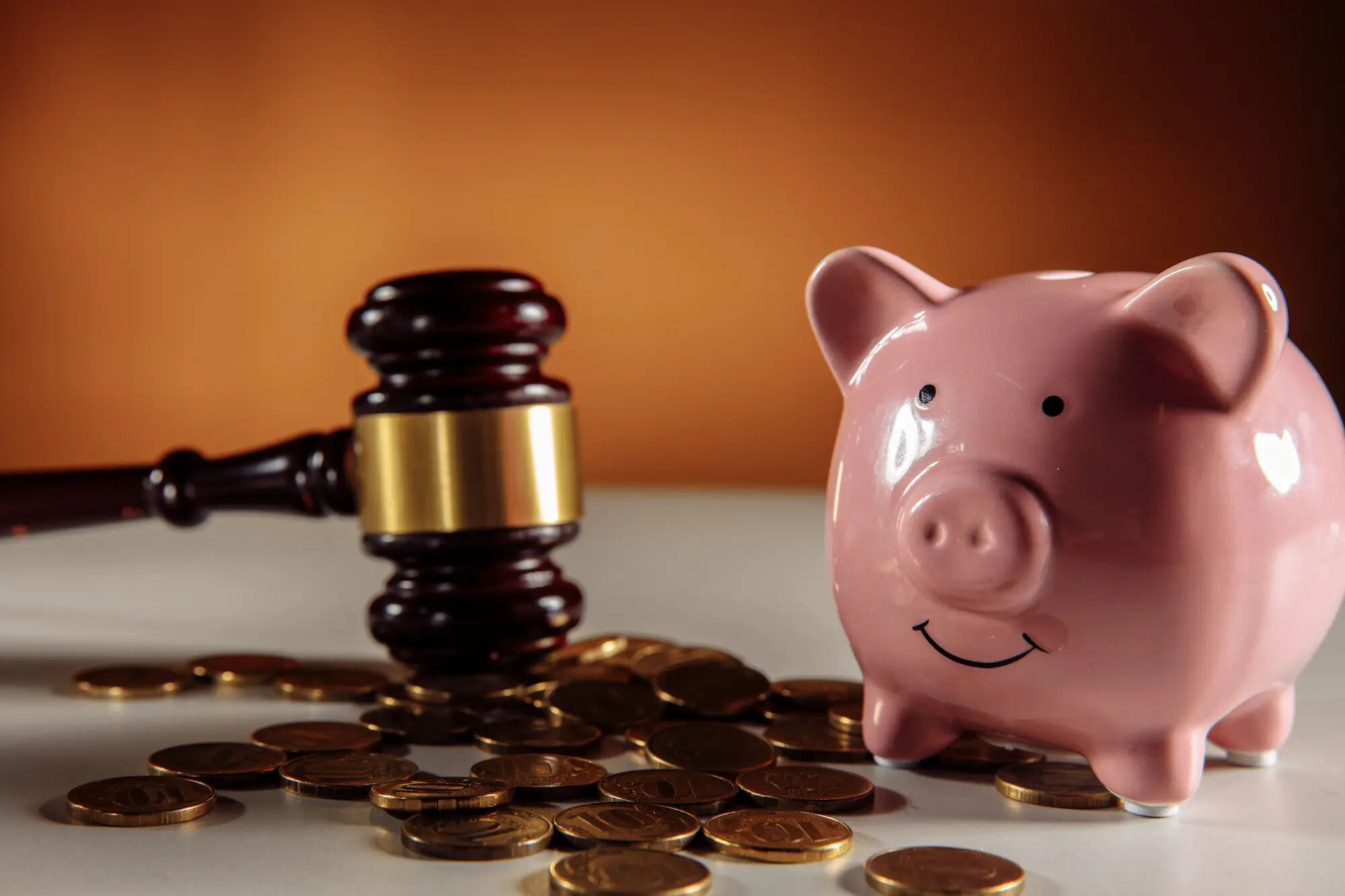 Ein hölzerner Richterhammer neben einem rosa Sparschwein und verstreuten Münzen auf einem Tisch – Symbol für Prozesskosten, Anwaltsgebühren und die finanziellen Aspekte von Rechtsstreitigkeiten.