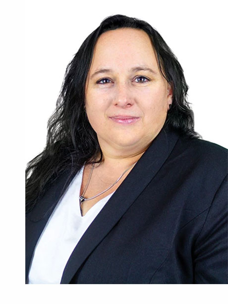 Frau mit dunklem Haar im Blazer lächelt vor weißem Hintergrund.