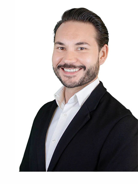 Mann mit dunklem Haar, Bart, schwarzem Blazer und weißem Hemd.