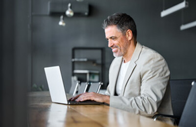 Makler sitzt lächelnd vor einem Laptop
