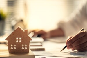 Modellhaus aus Holz neben einer Hand mit Stift