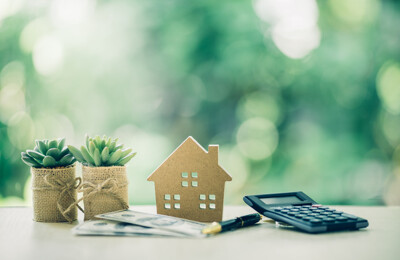 Kleines Modellhaus neben Taschenrechner, Unterlagen und kleinen Pflanzen