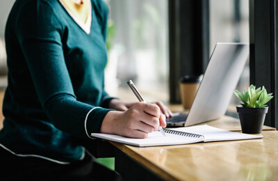 Frau sitzt mit Laptop am Tisch und macht sich Notizen