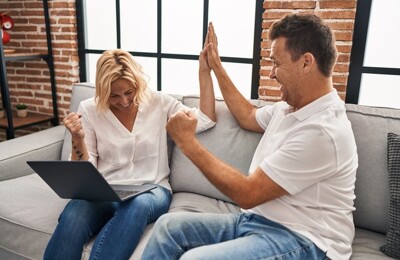 Ehepaar freut sich auf dem Sofa nach erfolgreichem digitalen Angebotsverfahren