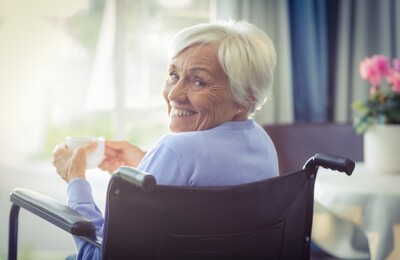 Seniorin sitzt in Stuhl und lächelt in die Kamera