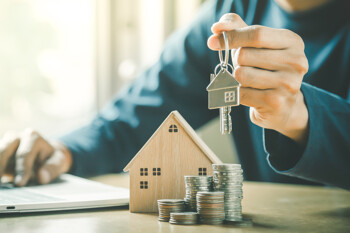 Mann hält Hausschlüssel vor Hausmodell und Münztürme