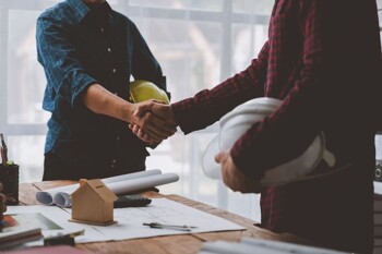 Zwei Männer geben sich über einem Schreibtisch mit Unterlagen die Hand