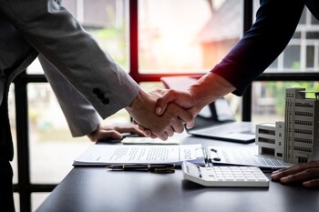 Zwei Männer geben sich über einem Schreibtisch mit Unterlagen die Hand