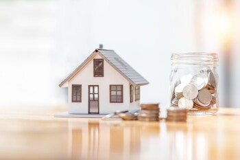 Glas mit Münzen neben Modellhaus