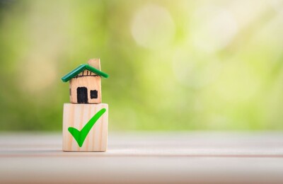 Ein Hausmodell steht auf einem Holzblock mit einem grünen Haken