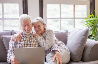 Ein älteres Ehepaar sitzt auf der Couch und schaut auf einen Laptop