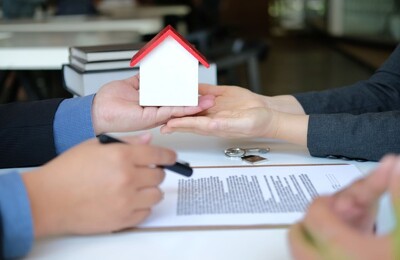 Ein Immobilieneigentümer übergibt ein Hausmodell an den neuen Besitzer