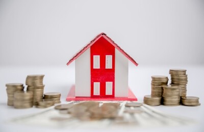 Ein Modellhaus steht zwischen Münzstapeln