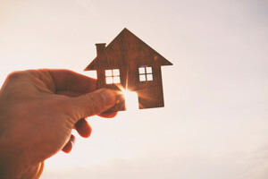 Hand hält ein Modellhaus in die Sonne