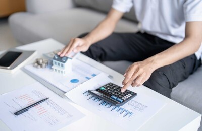 Person sitzt am Tisch mit Modellhaus und berechnet die Finanzierung