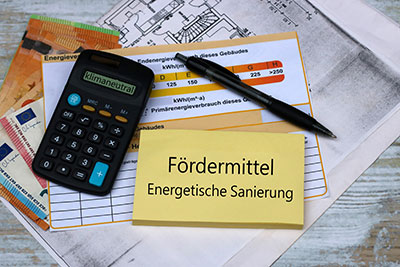 Zettel mit Aufschrift Fördermittel für energetische Sanierung, Modellhaus und Unterlagen
