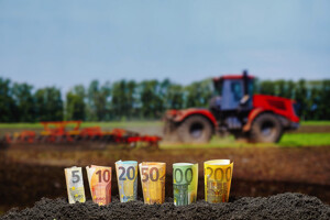 Eingerollte Geldscheine im Boden mit Traktor im Hintergrund