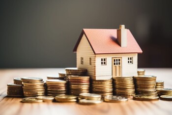 Hausmodell neben Geldmünzen