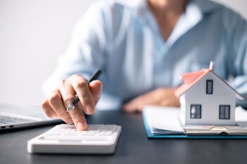 Makler mit Taschenrechner neben Hausmodell