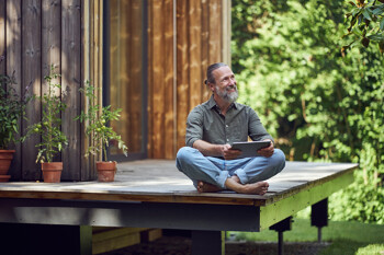 Mann sitzt auf der Terrasse seines Tiny Houses