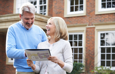 Ehepaar mit Immobilienmappe vor Haus