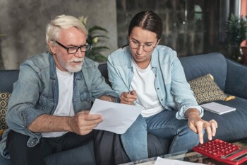 Eine Frau und ein Mann berechnen etwas mit Dokumenten und Taschenrechner