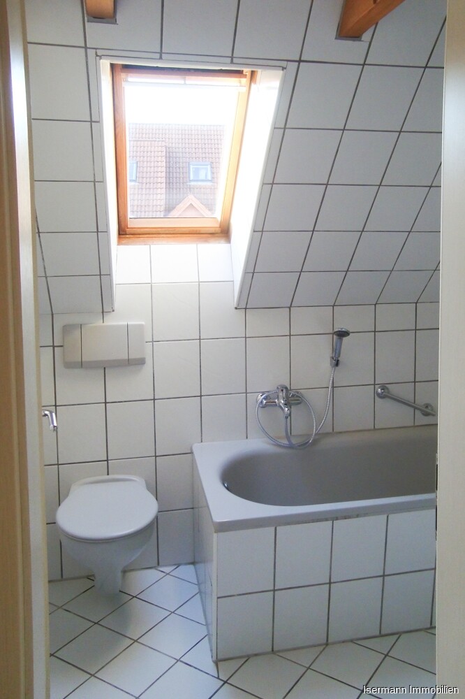 Das zeitlos weiß geflieste Badezimmer verfügt über eine Wanne.