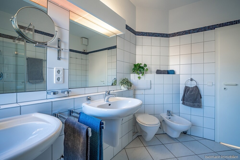 Der Raum ist klassisch weiß gefliest und mit zwei Waschbecken ausgestattet.