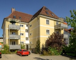 Das Mehrfamilienhaus aus westlicher Richtung mit Blick auf die Eingangstüre sowie die Parkplätze