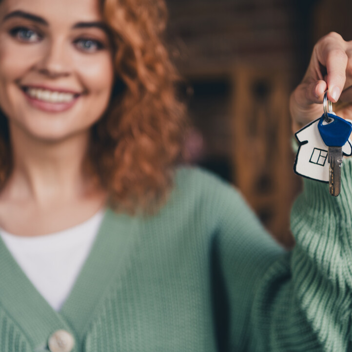 "Glückliche Frau mit Hausschlüssel in der Hand, Symbol für erfolgreichen Immobilienkauf, neues Zuhause.