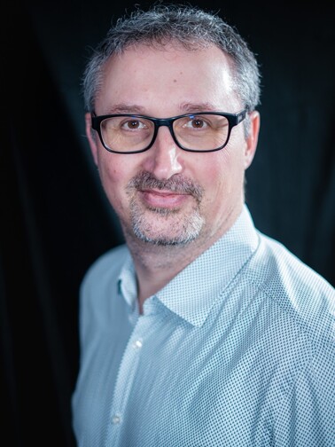 Porträt des Inhabers Andreas Langer, Professionelles Business-Porträt eines selbstbewussten Mannes mit Brille und grauem Haar. Er trägt ein hellblaues Hemd mit feinem Muster und hat einen freundlichen Ausdruck